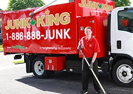 Junk King worker standing beside branded red dump truck.